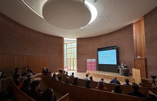 RSAW architecture conference speaker in a circular lecture hall with screen and window at side