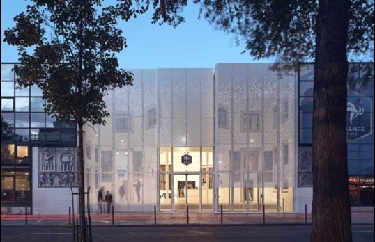 Modern square building with full height glass frontage set behind metal cutout panels.