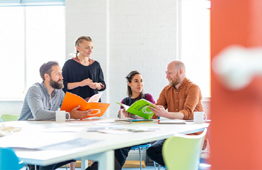 Four adults in a well light room sat around a table looking at brightly coloured RIBA Contract books