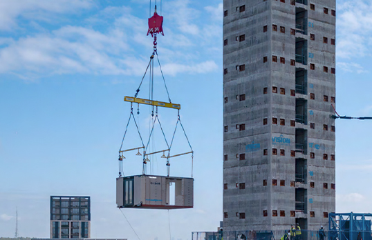 Crane lifting large container with tall building under construction in the background