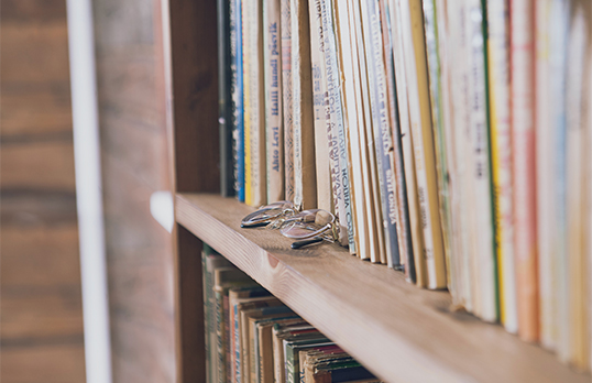 Rows of thin journals and books on a wooden shelf with a pair of glasses at the front of the shelf