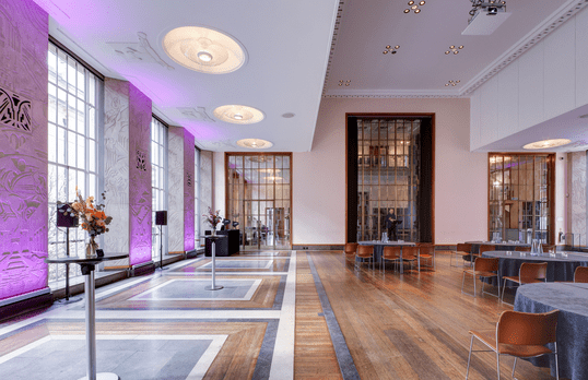 Florence Hall with round table set up, floor to ceiling Art Deco windows and ceiling details backlight with a soft purple light