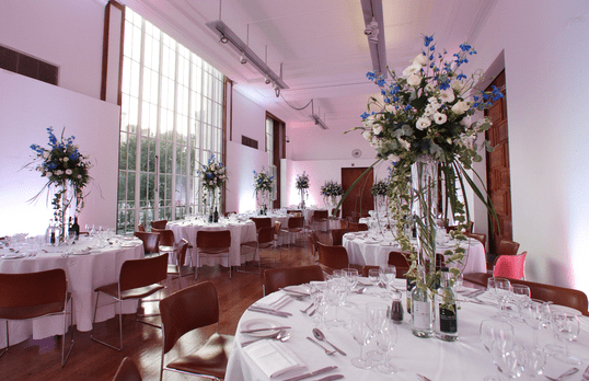 Round set tables with tall floral centre pieces in the RIBA Gallery with floor-to-ceiling window