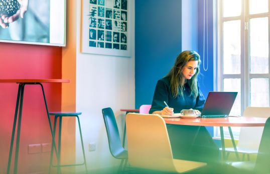 Woman sitting in a cafe working from her laptop and taking notes
