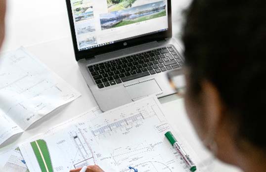 Person looking at architecture plans on paper and on a laptop screen