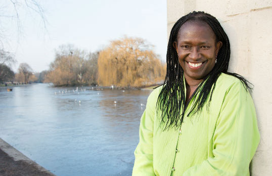 Elsie Owusu sitting in front of a lake with willows and birds in the distance