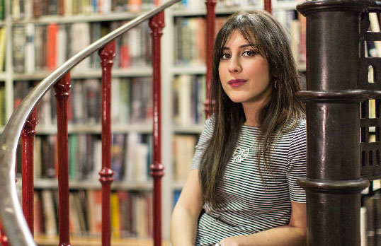 Maral Rahmantalab sitting on a spiral staircase in front of a wall of books