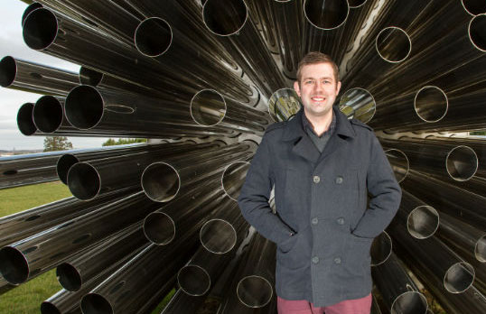 Stephen Ware standing in front of a large architectural structure which comprises steel tubing radiating on all sides from a central point