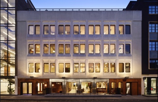 Façade of white square building  with rectangular windows  lit up at dusk.