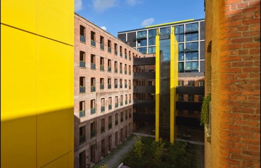 Brown brick building with grid of square cout out windows with bright yellow clad tower stairwells.