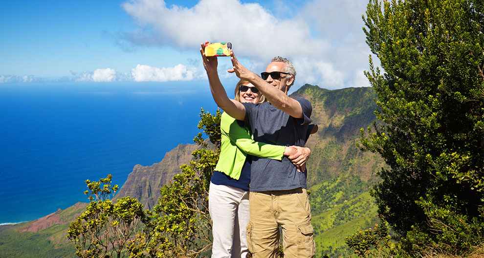 a man and women take a selfie on a mountainside overlooking a deep blue sea