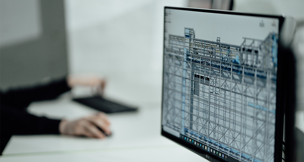 Desktop computer display with detailed architecture drawing and person using mouse/keyboard in the background out of focus