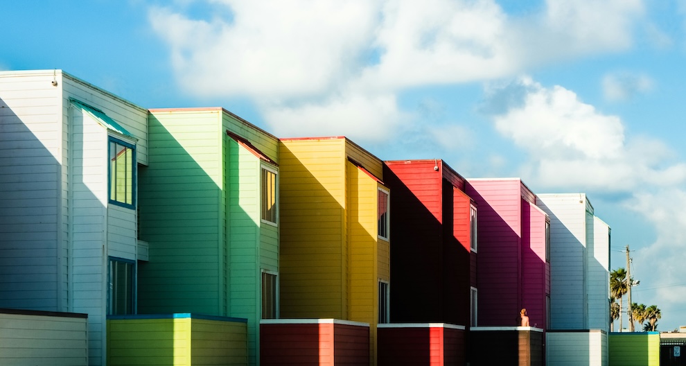 Row of staggered houses each a different colour - blue, green, yellow, red, pink, pale blue